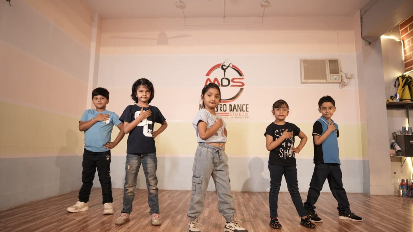 Kids striking a pose in front of the Maestro Dance Studio wall