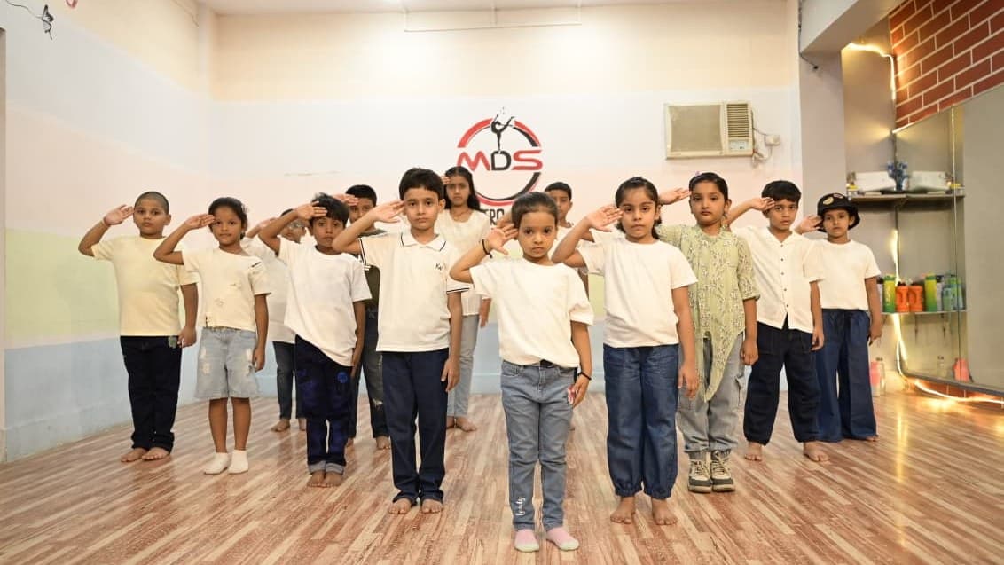 A larger kids batch saluting together in front of the studio wall