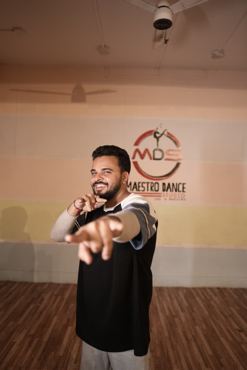 An instructor at Maestro Dance Studio, in front of the studio's painted logo wall